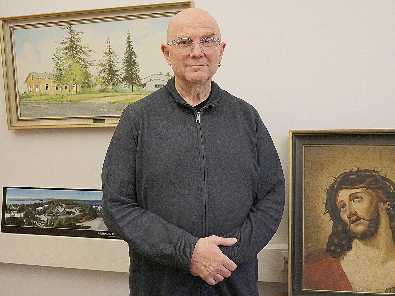 Nurmeksen uusi kirkkoherra Juhani Saastamoinen muutti Valtimolta Nurmekseen tänä kesänä. Työhuoneen seinällä näkyy taulu uudesta kodista, Nurmeksen Pappilasta.
