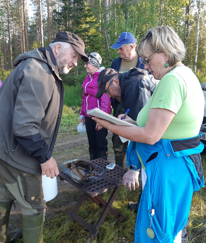 Punnitus käynnissä. Urpo Lehikoinen punnitsee Pauli Pesosen (vas.) kalasaalista. Sirpa Lehikoinen kirjaa tuloksen vihkoon. Taustalla Raija Karhapää ja Pekka Turunen.