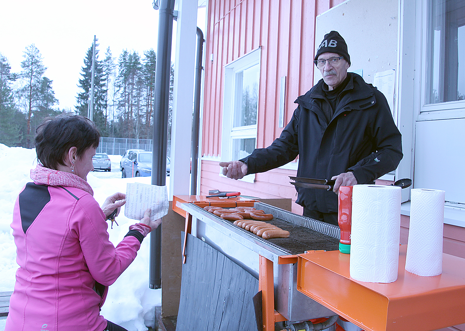 Osanottomaksuun kuului juotavan lisäksi niin suolaista kuin makeaakin syötävää. Makkara maistui hiihdon jälkeen Sisko Pekkariselle. Grillimestarina hääri Mikko Halonen. 